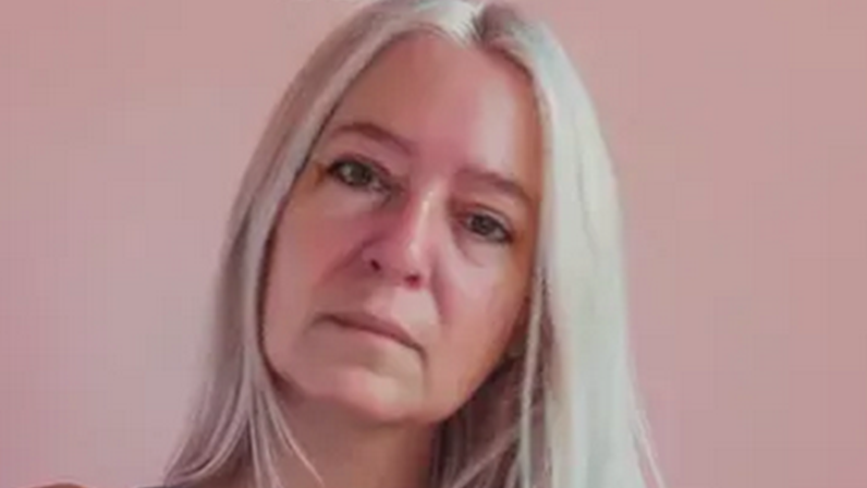 A headshot photo of a white-haired woman looking into camera with head cocked.