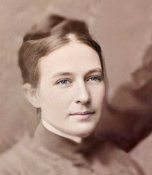 A black and white headshot photo of a woman wearing a high collar, with hair in a bun.