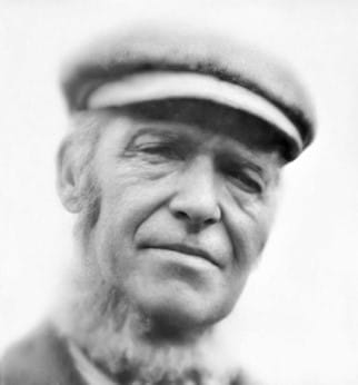 A headshot photo of a man with beard below the chin, wearing a cap.