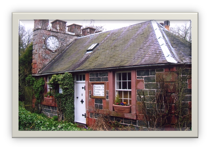 A photo of a stone cottage with shingled roof and clock on the massive chimney spanning the width of the building.