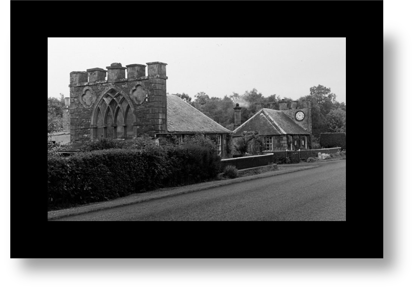 A photo of a stone cottages with shingled rooves, each with chimneys spanning the width of the buildings, one with ornate windows and the other a clock.