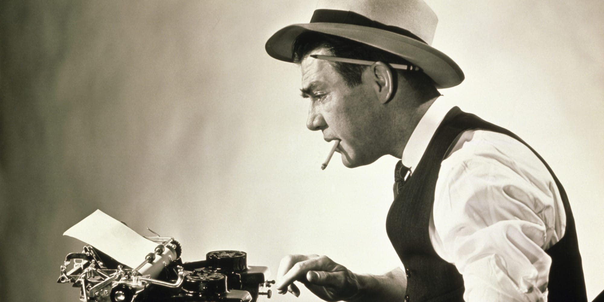 A profile view image of a newspaper man in shirtsleeves, vest, and hat, with cigarette and pencil behind ear typing on a vintage typewriter.