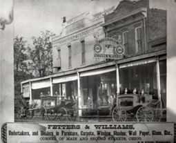 A streetfront photo of an undertaker's business, with horse-drawn hearses.