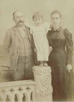 A family portrait of parents with one child standing between them on a pillar.