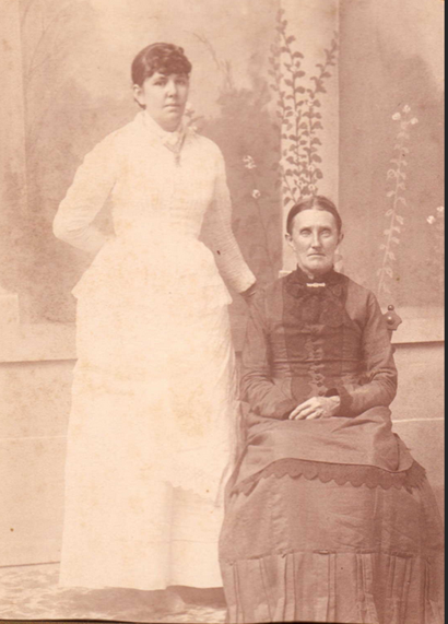 Portrait photograph of two women, one seated, in formal attire.