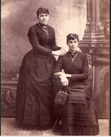 Portrait photograph of two women, one seated, in formal attire.